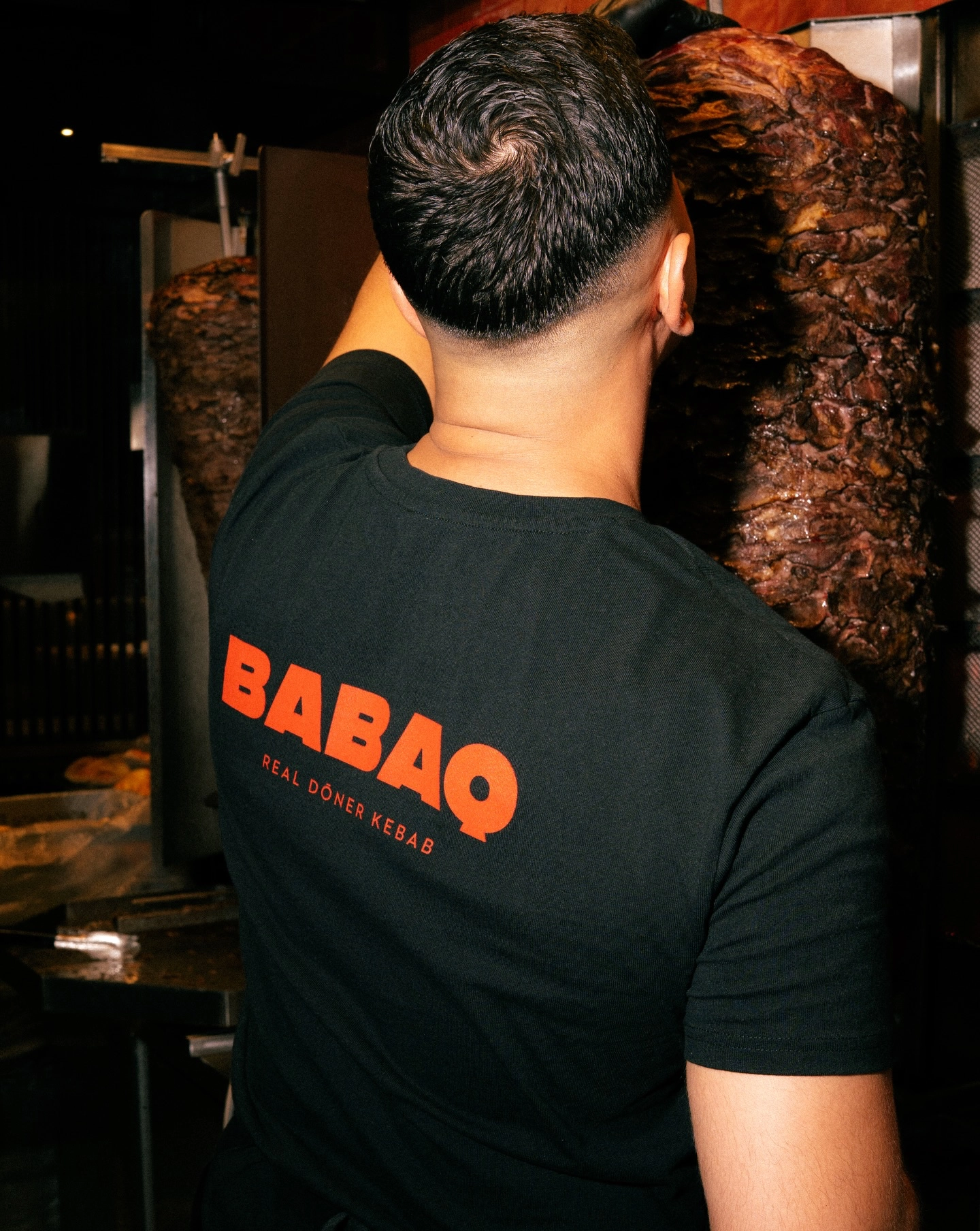 BABAQ Mitarbeiter bereitet Döner am Drehspieß zu, Logo sichtbar
